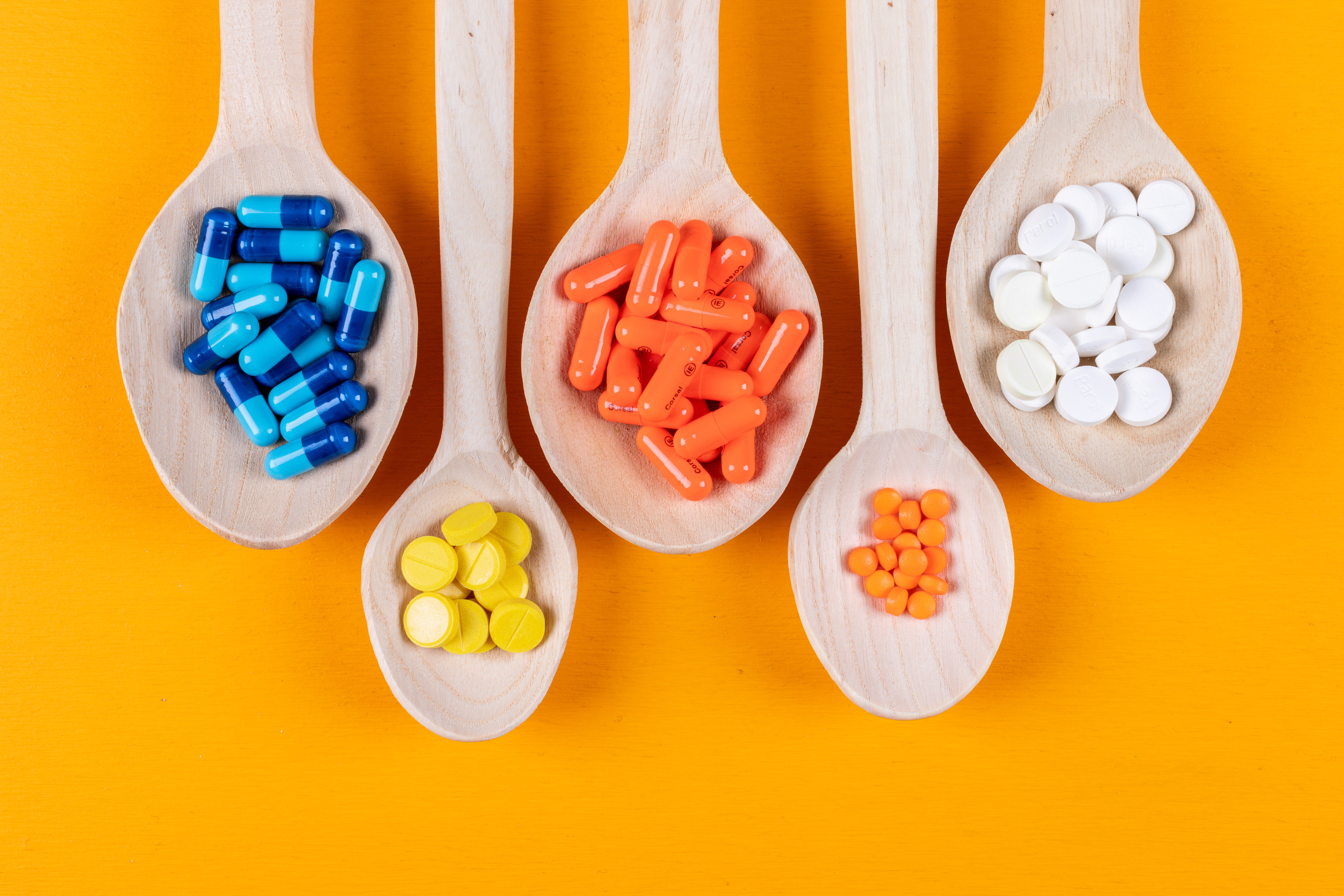 top-view-colorful-pills-wooden-spoons-orange-background-horizontal.jpg
